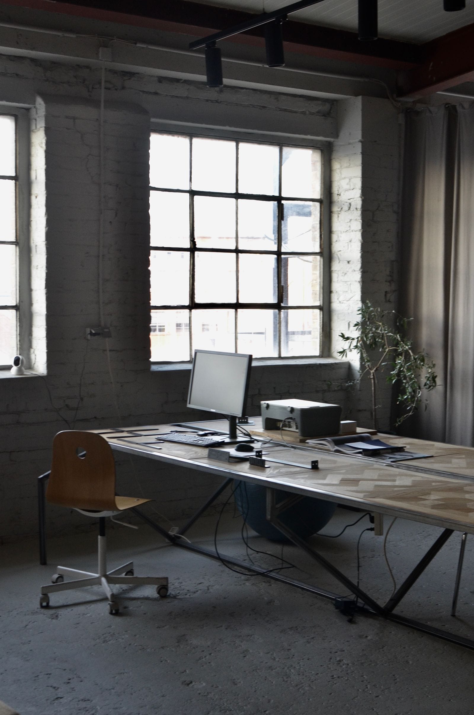 A desk and computer under tall steel windows in a converted factory