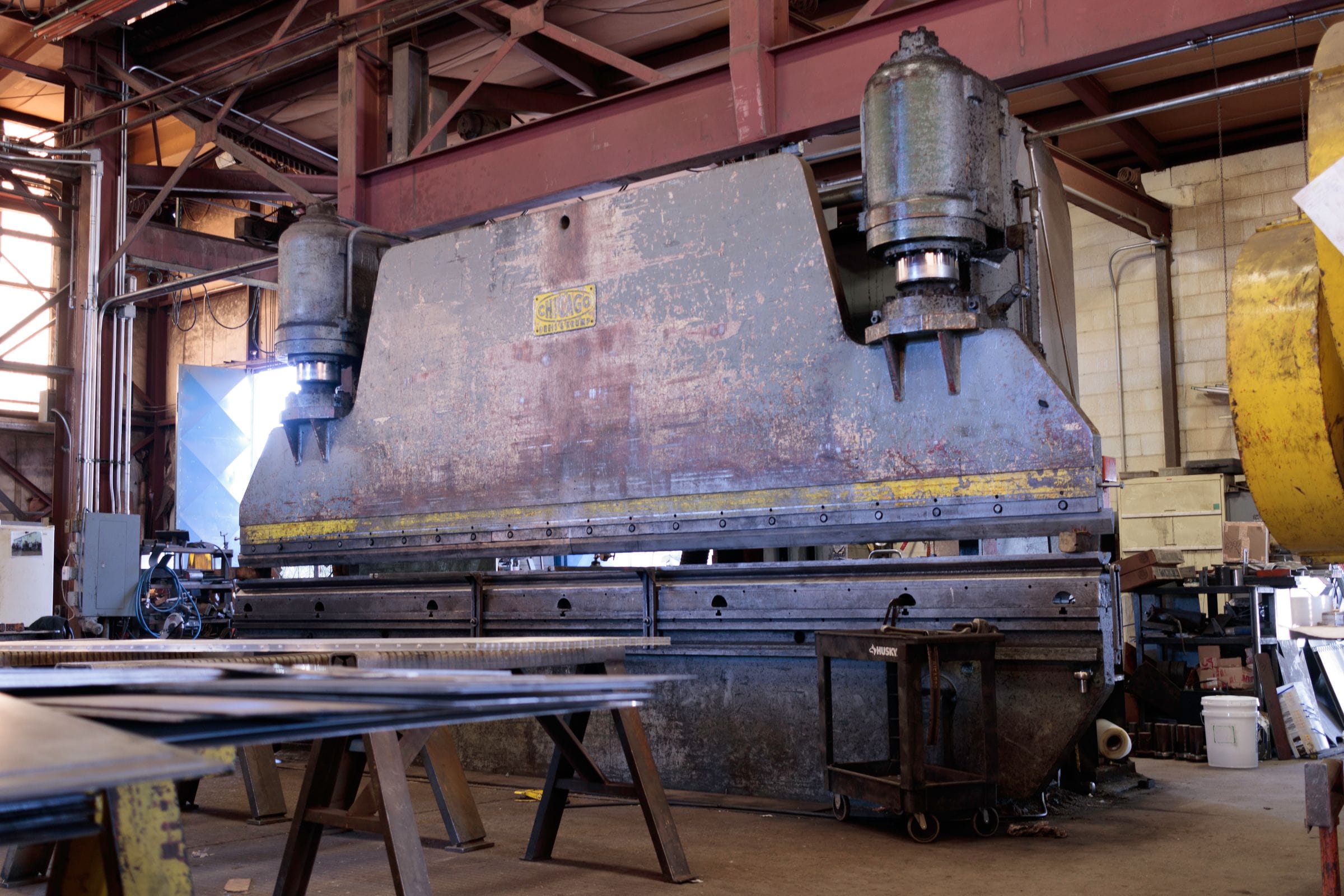 A heavy press brake in a metal workshop, sheet stock on the table