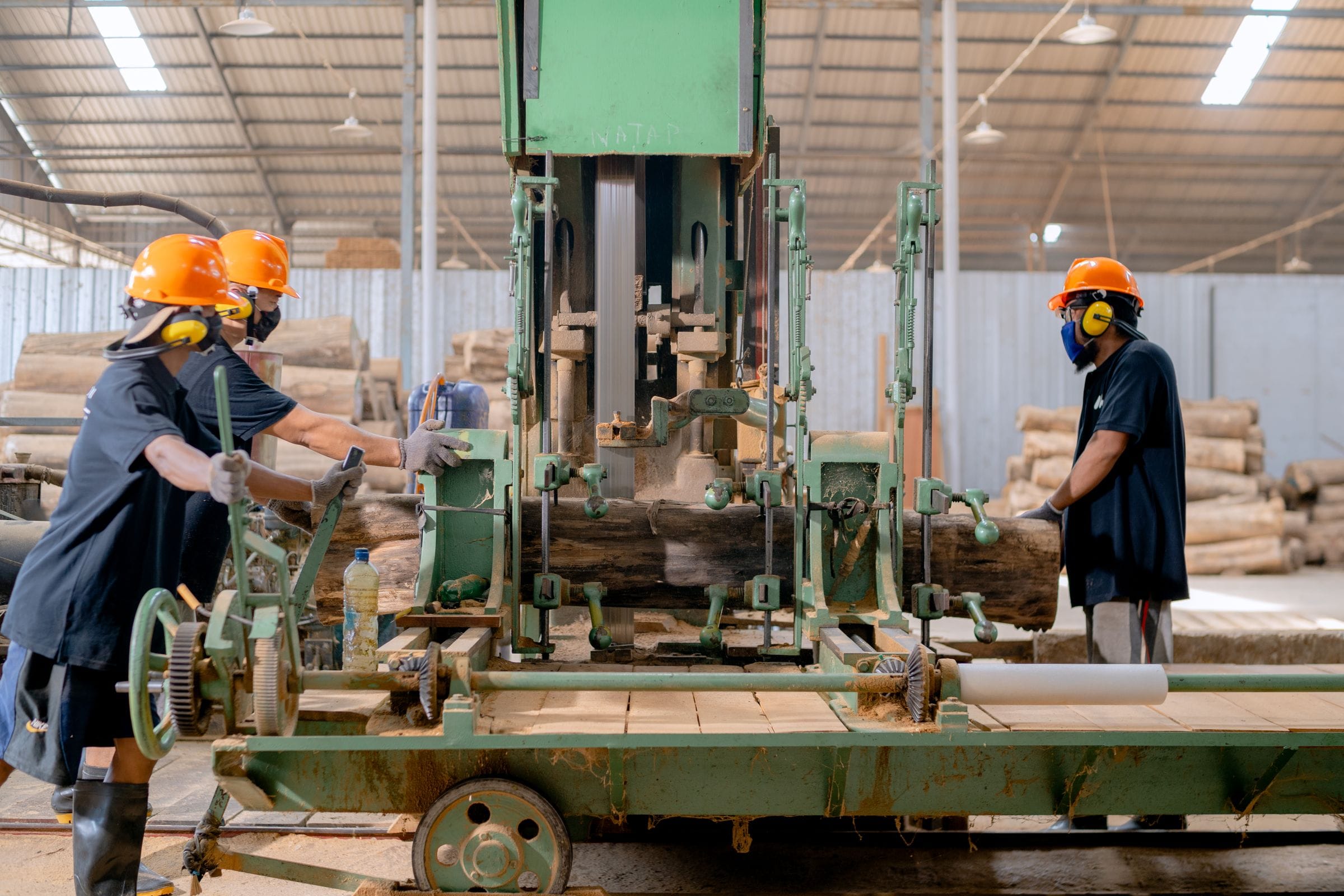 Workers feeding timber through a saw in a large production hall