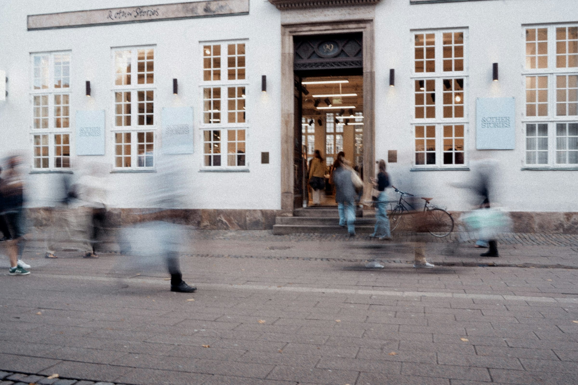 Lidé procházejí kolem obchodu a vcházejí dovnitř, rozmazaní v pohybu